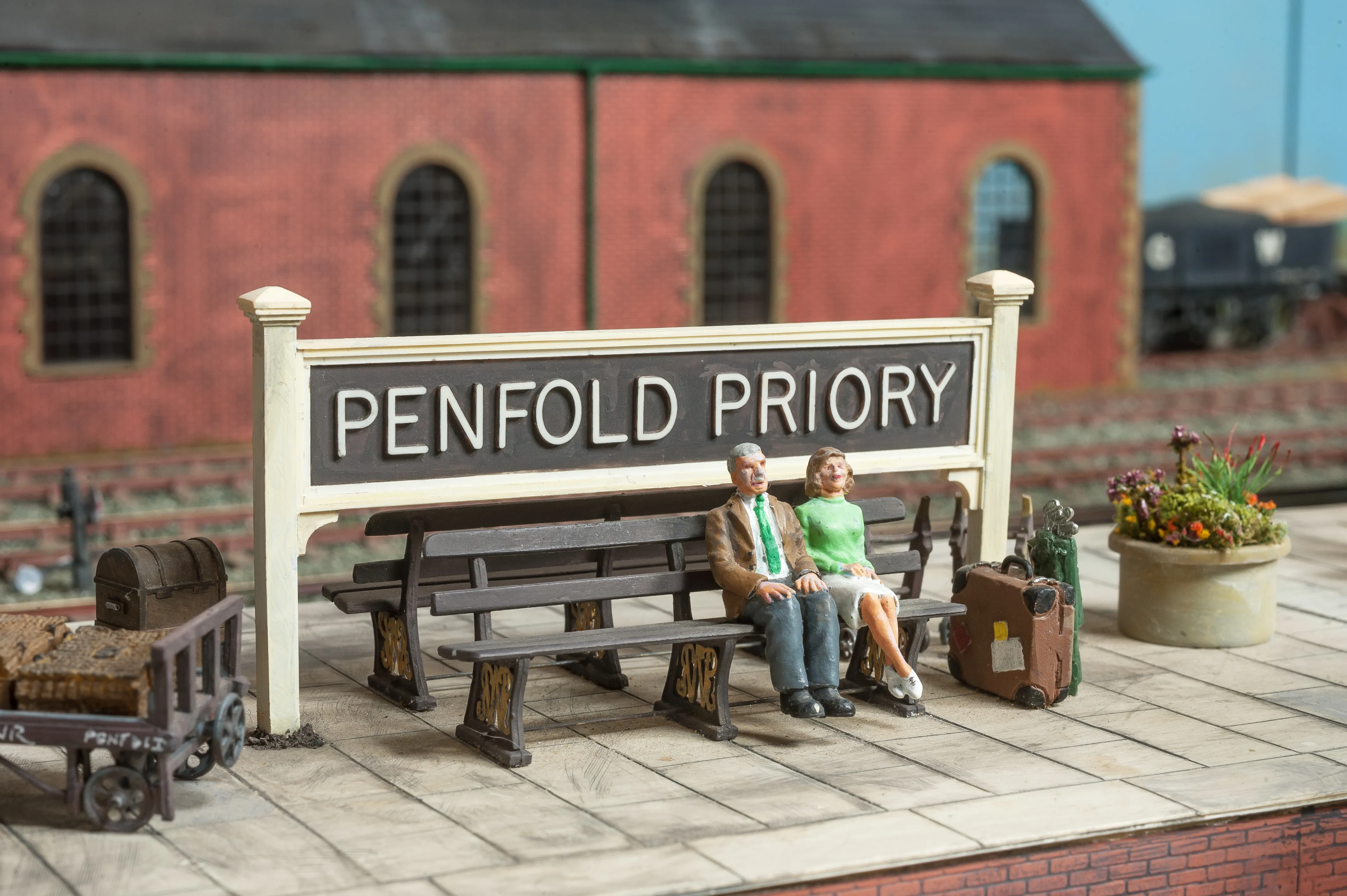 Close up of Penfold Priory station platform with two people sat on a bench